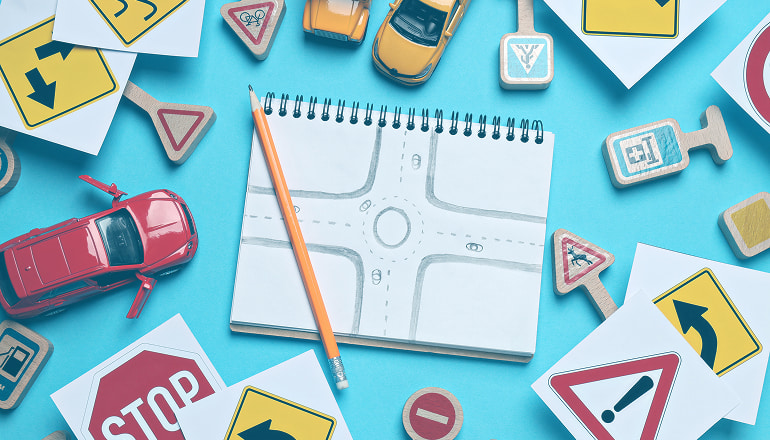 Libreta con dibujo de carretera representando ejemplos de indemnización por accidente de tráfico, un lápiz al lado y señales de tráfico al rededor